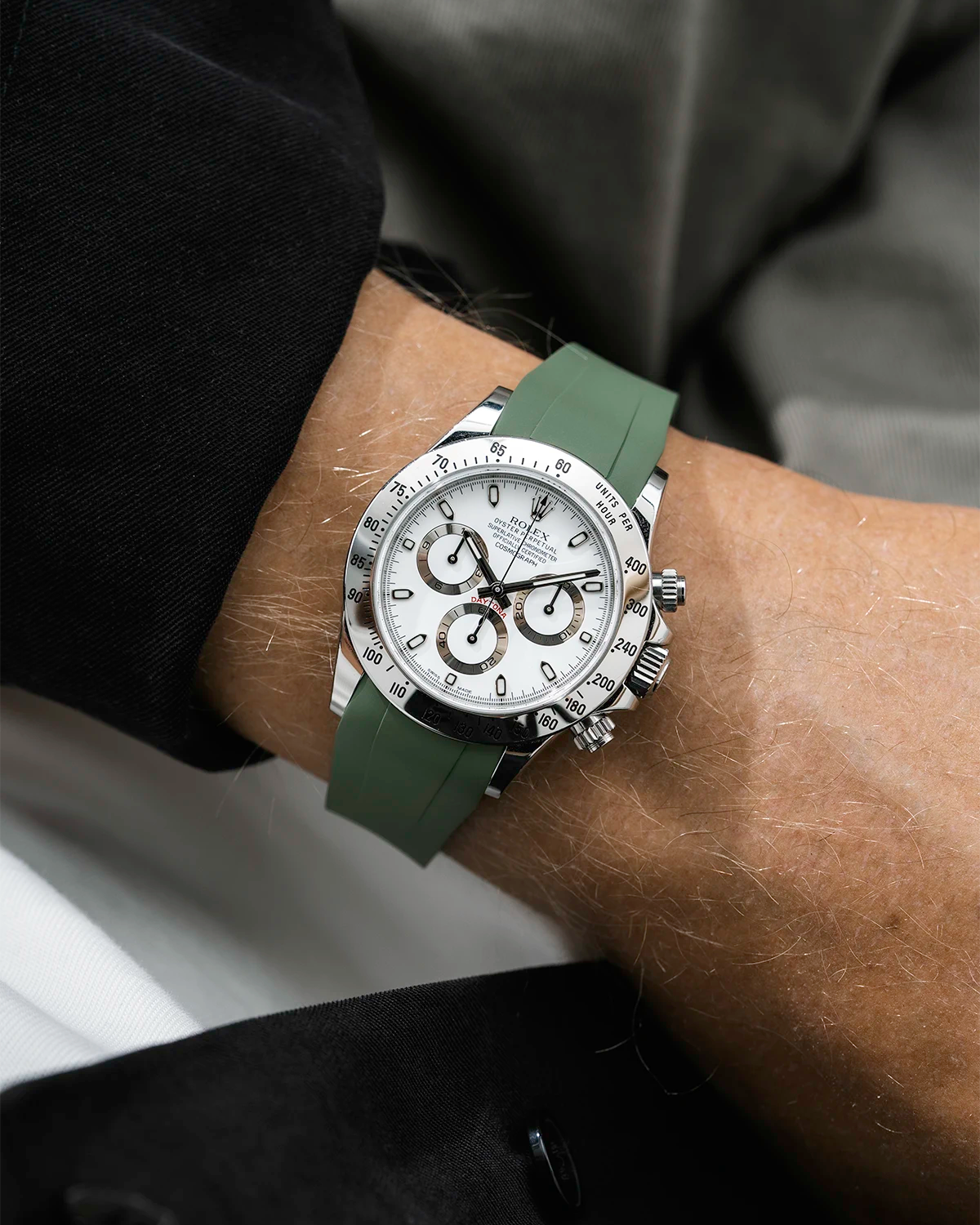 Close-up of a person wearing a white Rolex Daytona watch with a black jacket sleeve and a green FKM rubber watch strap from Wristbuddys