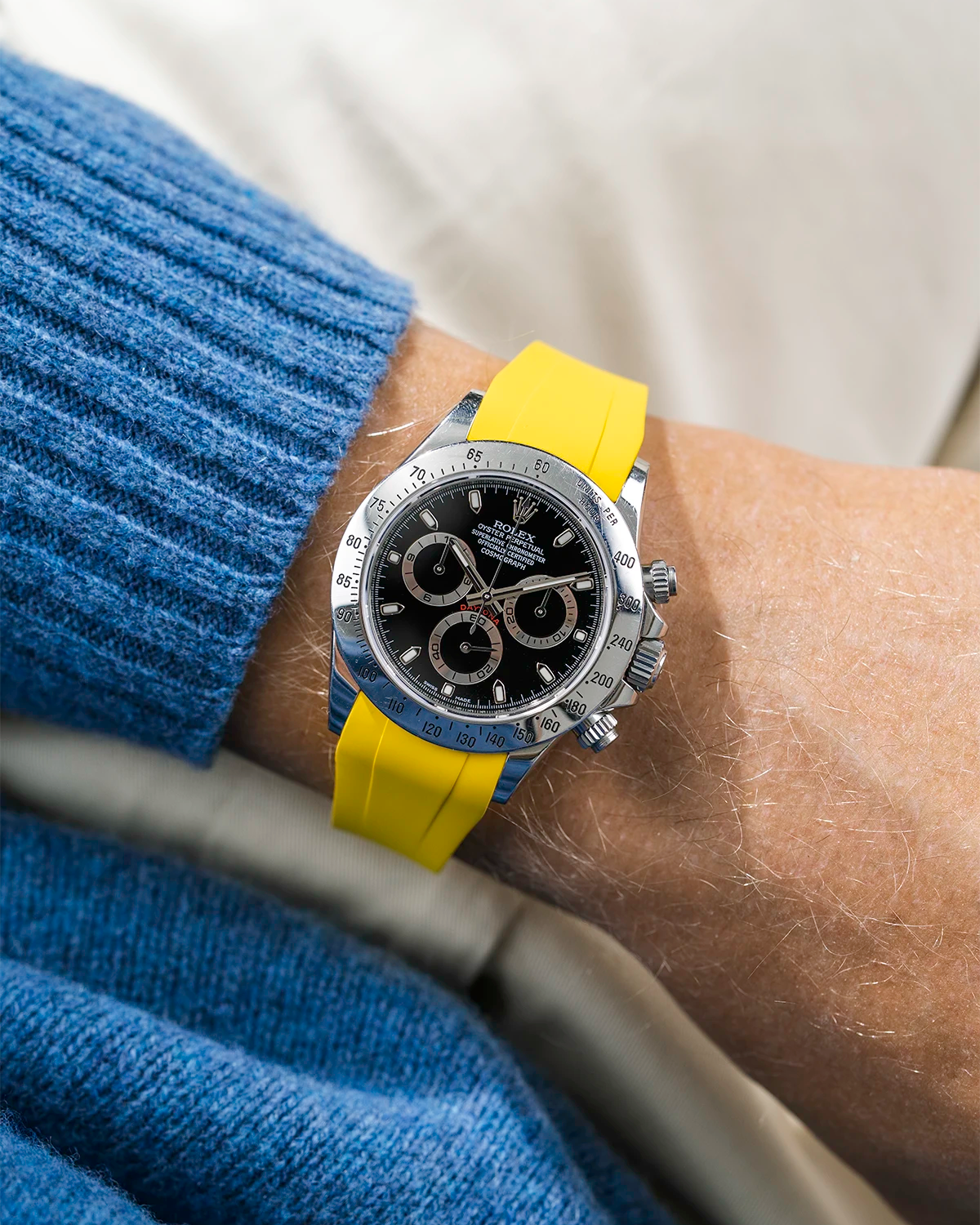Close-up of a person wearing a black Rolex Daytona watch with a blue jacket sleeve and a yellow FKM rubber watch strap from Wristbuddys