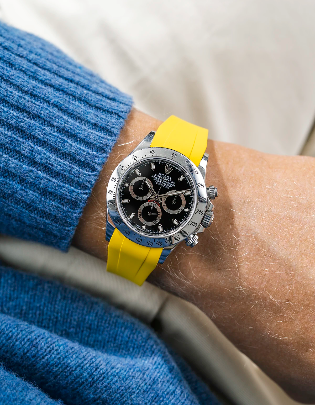 Close-up of a person wearing a black Rolex Daytona watch with a blue jacket sleeve and a yellow FKM rubber watch strap from Wristbuddys
