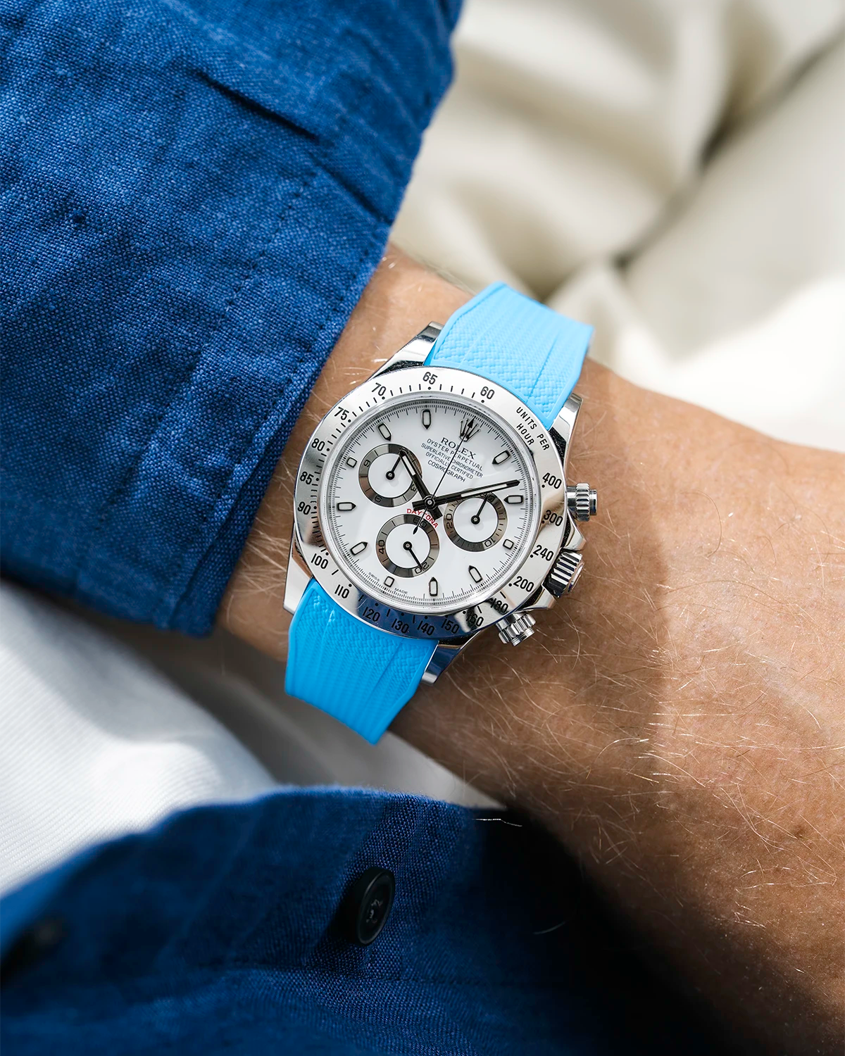 Close-up of a person wearing a white Rolex Daytona watch with a blue stiped shirt sleeve and a tuquoise vertech FKM rubber watch strap from Wristbuddys
