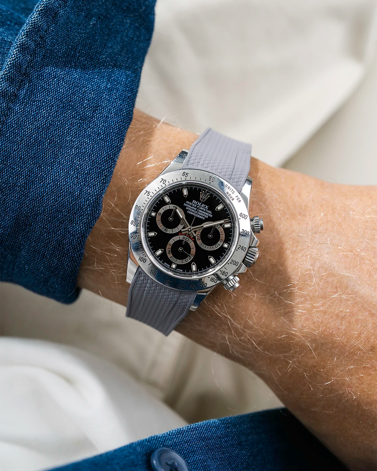 Close-up of a person wearing a black Rolex Daytona watch with a blue stiped shirt sleeve and a grey vertech FKM rubber watch strap from Wristbuddys