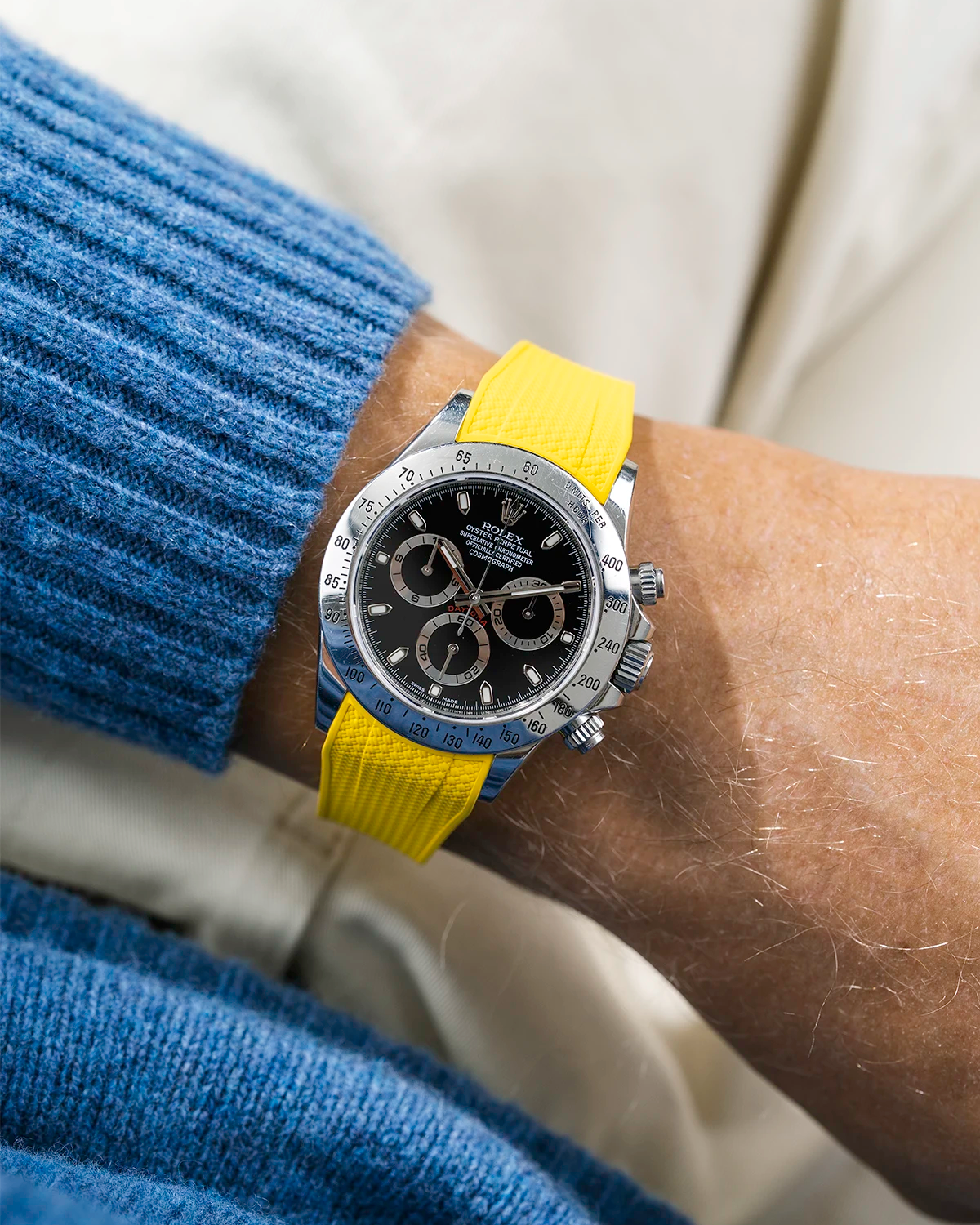 Close-up of a person wearing a black Rolex Daytona watch with a blue wool sweatshirt and a yellow vertech FKM rubber watch strap from Wristbuddys