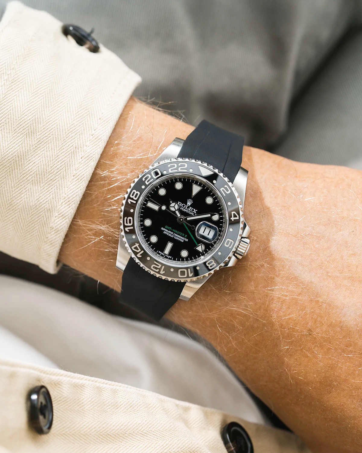 Close-up of a person wearing a Rolex GMT Master Green hand 116710 model watch with beige jacket sleeve and a black FKM rubber watch strap from Wristbuddys