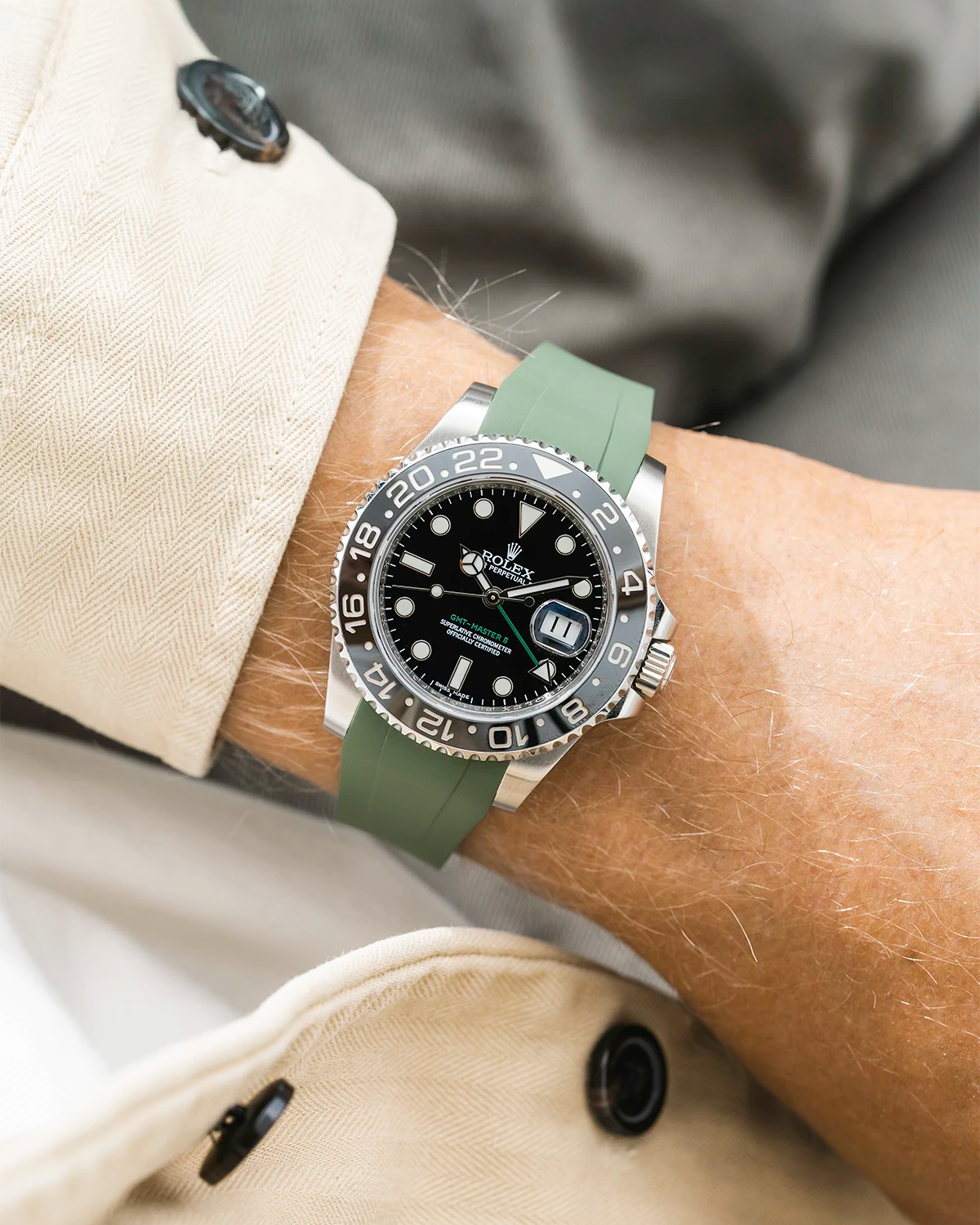 Close-up of a person wearing a Rolex GMT Master Green hand 116710 model watch with beige jacket sleeve and a military green FKM rubber watch strap from Wristbuddys