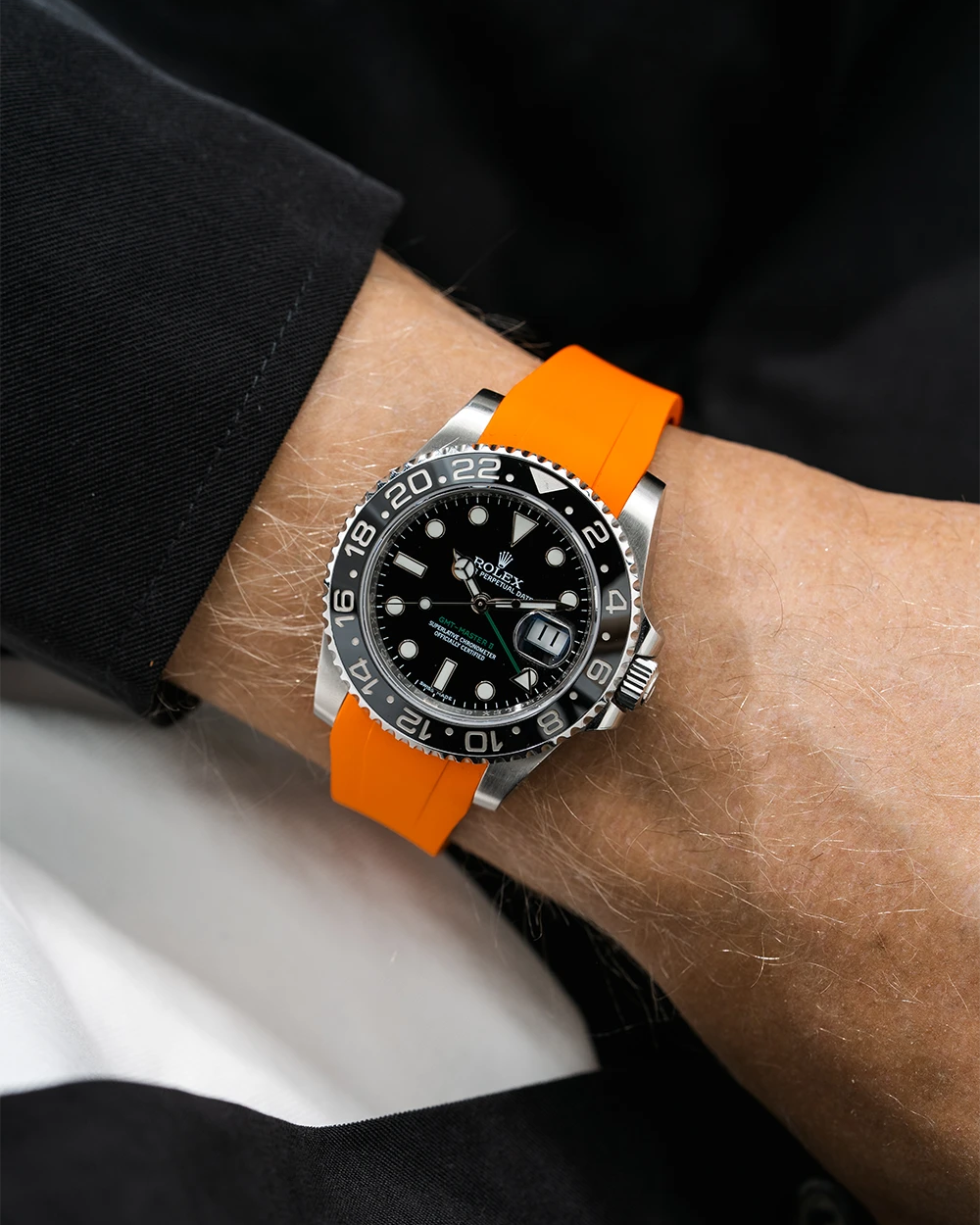 Close-up of a person wearing a Rolex GMT Master Green hand 116710 model watch with black jacket sleeve and a orange FKM rubber watch strap from Wristbuddys