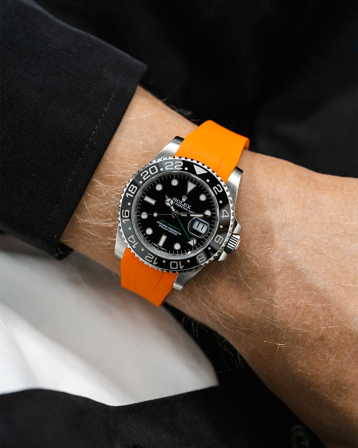 Close-up of a person wearing a Rolex GMT Master Green hand 116710 model watch with black jacket sleeve and a orange FKM rubber watch strap from Wristbuddys