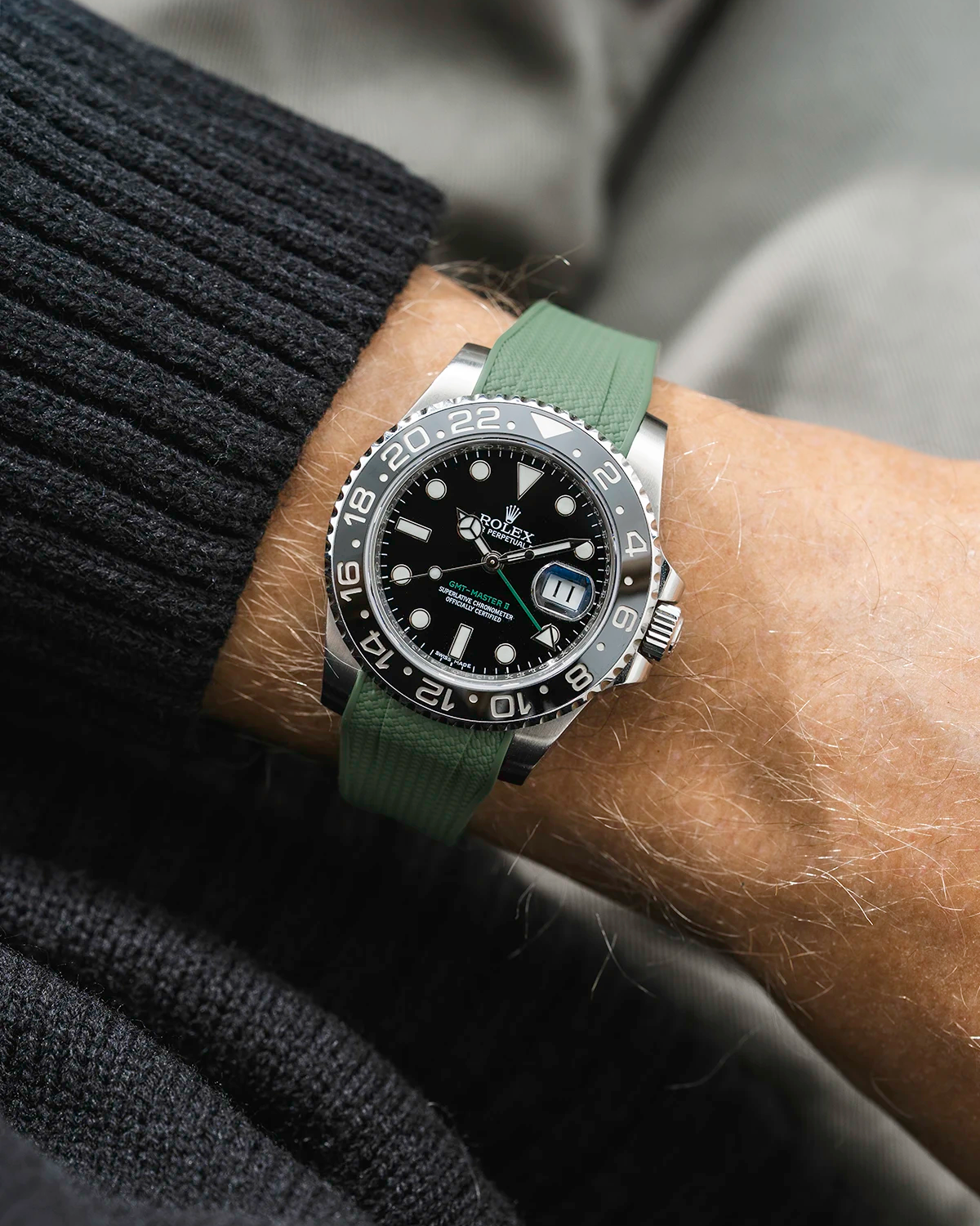 Close-up of a person wearing a Rolex GMT Master Green hand 116710 model watch with black jacket sleeve and a green vertech FKM rubber watch strap from Wristbuddys