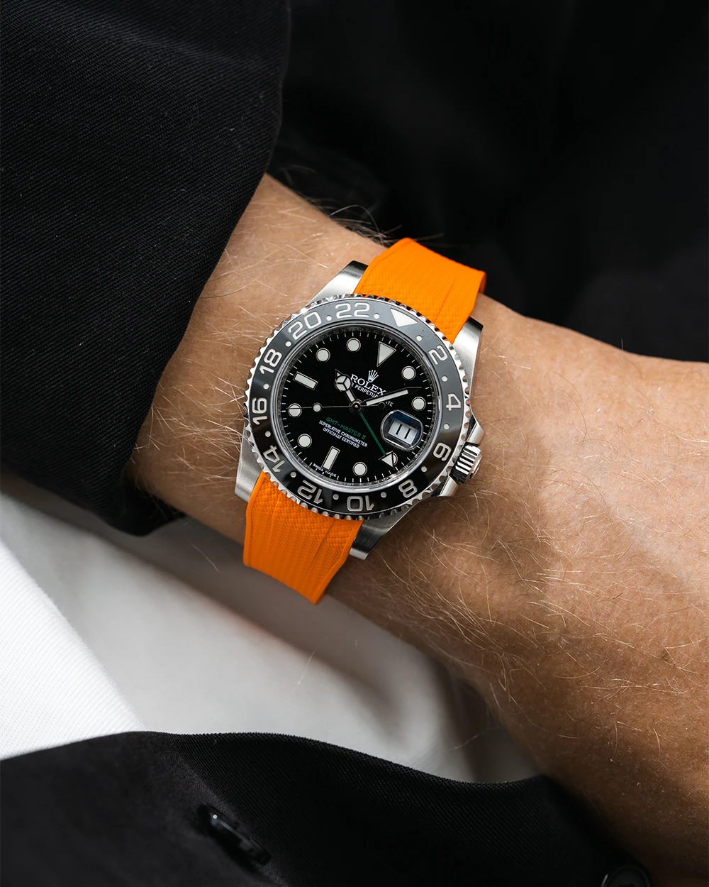 Close-up of a person wearing a Rolex GMT Master Green hand 116710 model watch with black jacket sleeve and a orange vertech FKM rubber watch strap from Wristbuddys