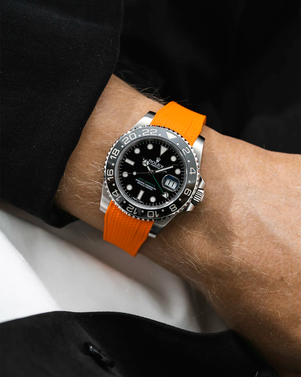 Close-up of a person wearing a Rolex GMT Master Green hand 116710 model watch with black jacket sleeve and a orange vertech FKM rubber watch strap from Wristbuddys
