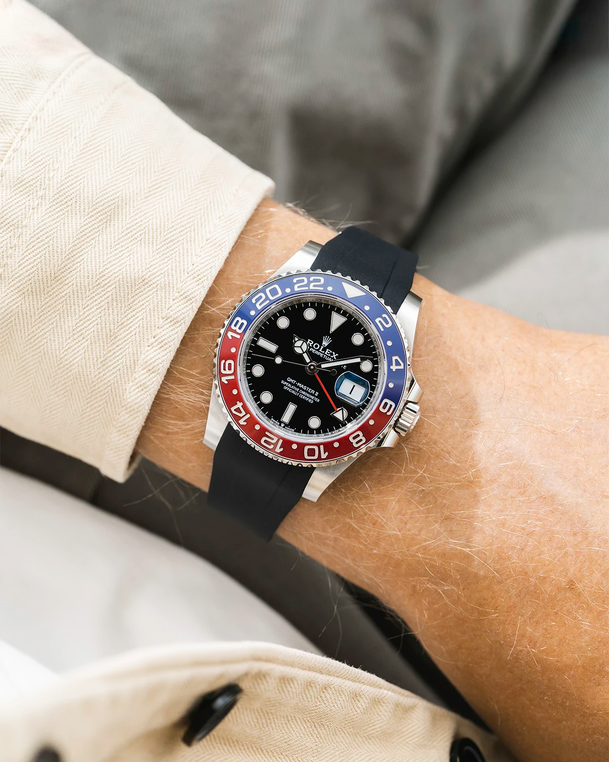 Close-up of a person wearing a Rolex GMT Master 2 Pepsi model watch with a beige jacket sleeve and a black FKM rubber watch strap from Wristbuddys