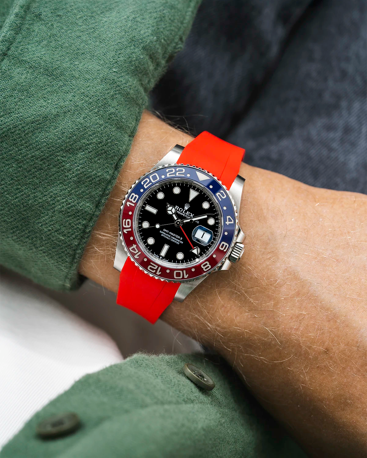 Close-up of a person wearing a Rolex GMT Master 2 Pepsi model watch with a green jacket sleeve and a red FKM rubber watch strap from Wristbuddys