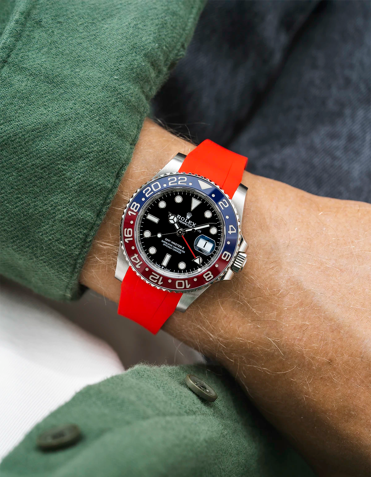 Close-up of a person wearing a Rolex GMT Master 2 Pepsi model watch with a green jacket sleeve and a red FKM rubber watch strap from Wristbuddys