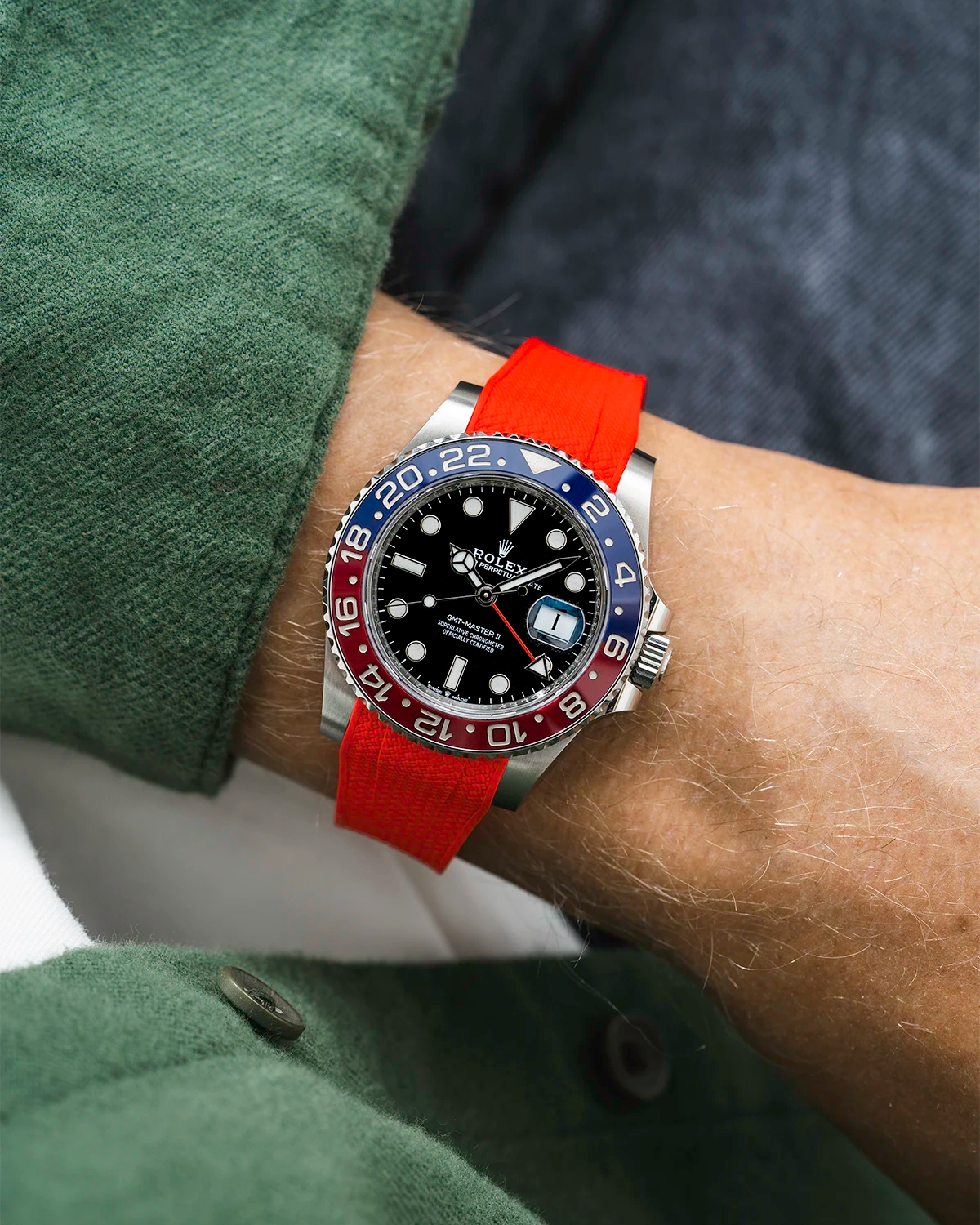 Close-up of a person wearing a Rolex GMT Master 2 Pepsi model watch with green jacket sleeve and a red vertech FKM rubber watch strap from Wristbuddys