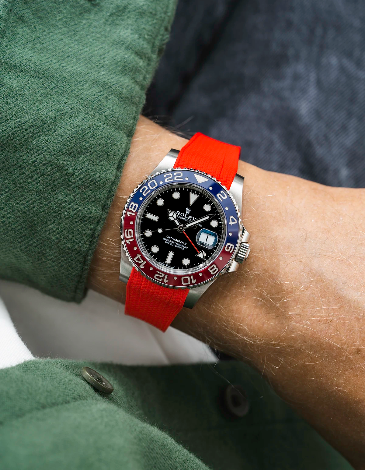Close-up of a person wearing a Rolex GMT Master 2 Pepsi model watch with green jacket sleeve and a red vertech FKM rubber watch strap from Wristbuddys