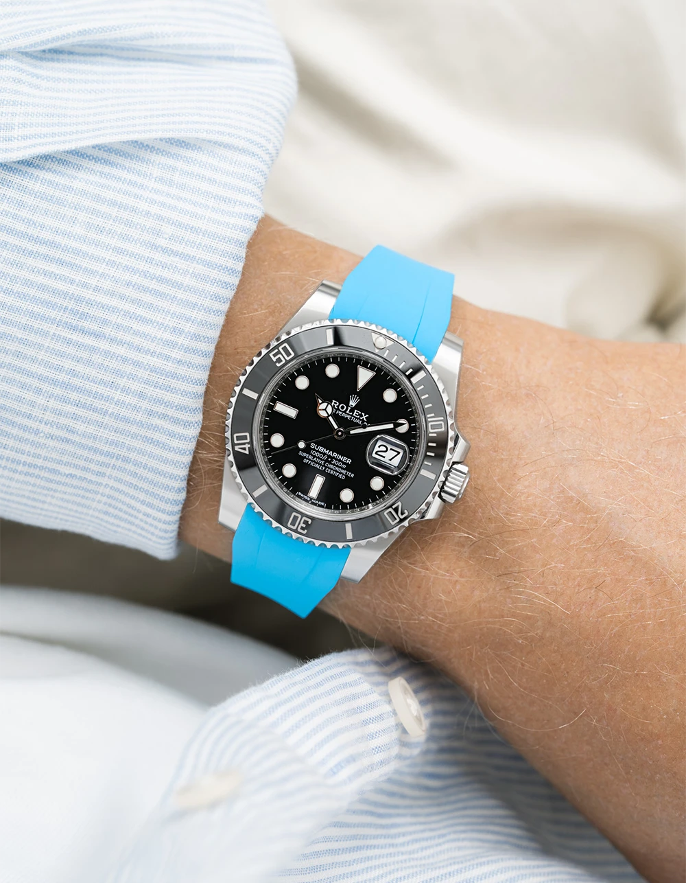 Wrist wearing a Rolex Submariner on a capri blue Wristbuddys FKM Rubber watch strap and white shirt background