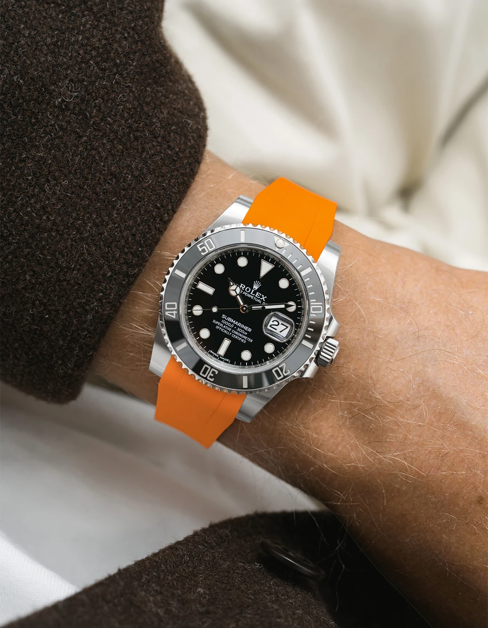Wrist wearing a Rolex Submariner on a Wristbuddys FKM Rubber watch strap with an orange strap on a neutral background