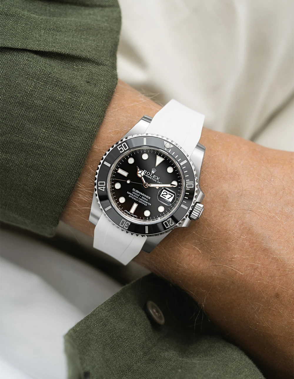 Close-up of a wrist wearing a Rolex Submariner on a wjote Wristbuddys FKM Rubber strap, green sleeve, and beige background.