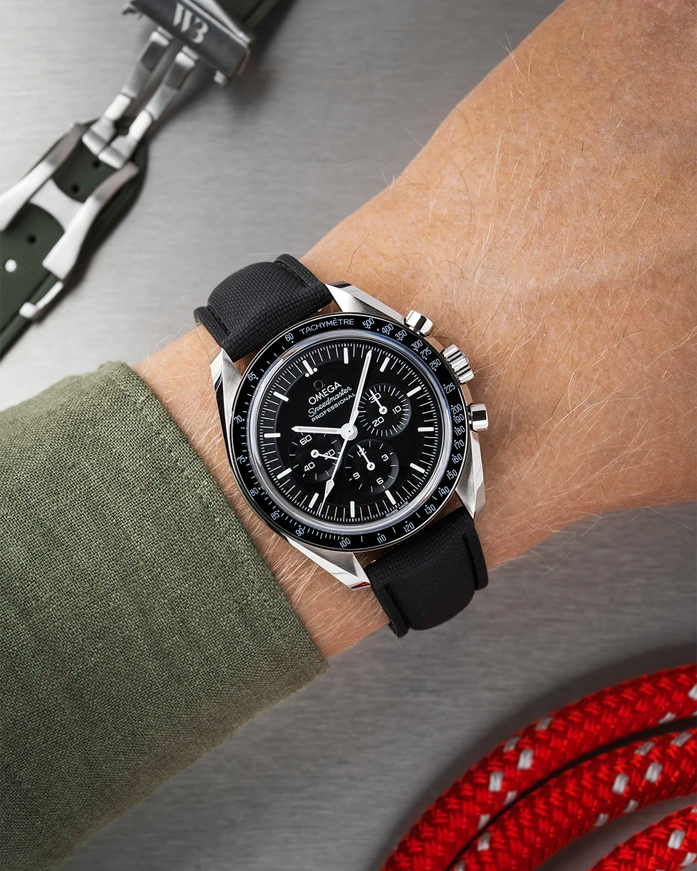 Black Omega Speedmaster with a detailed face on a person's wrist, with a blurred background