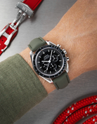 Wrist wearing a black Omega Speedmaster  with a detailed face on a wrist with a green sleeve.