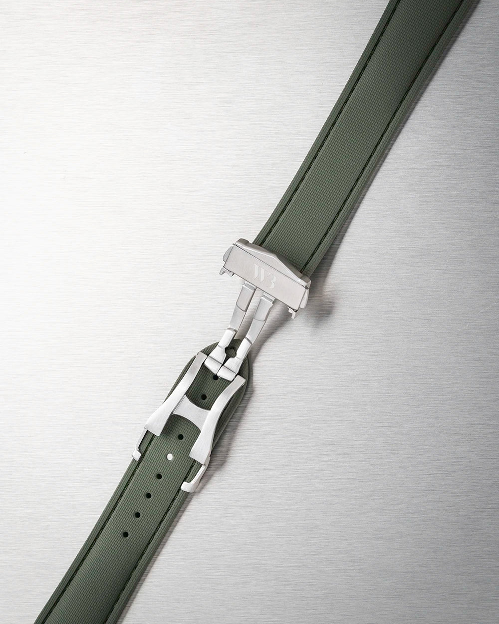 Close-up of a black watch strap with a silver buckle on a metallic background