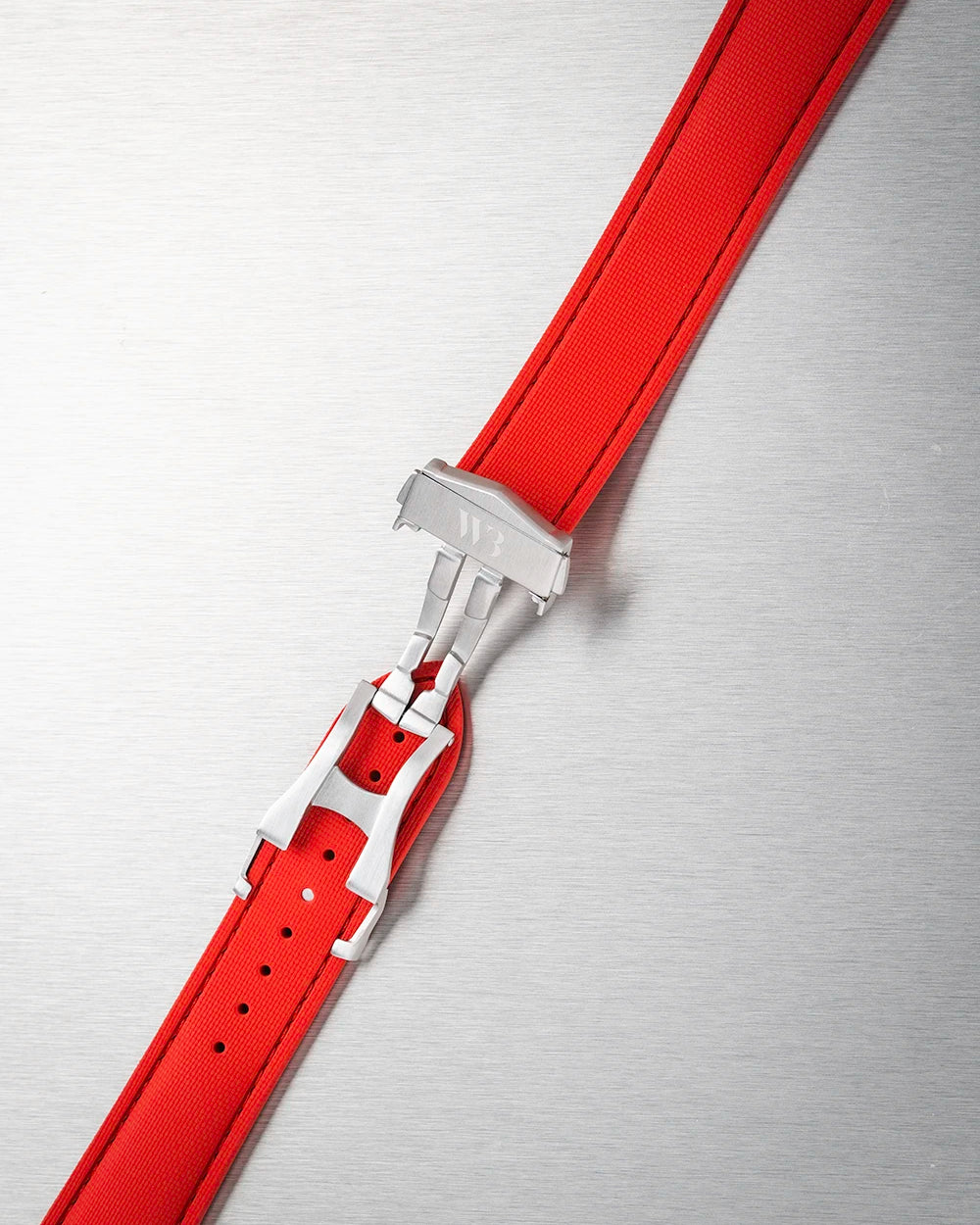 Red rubber watch strap with silver buckle on a metallic surface