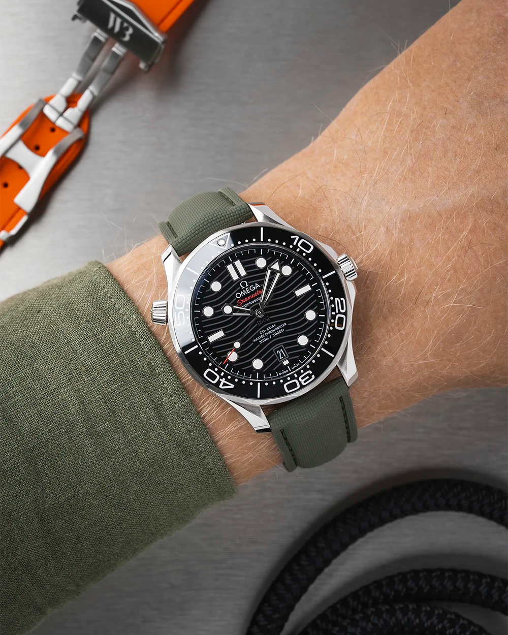 Wrist wearing a black Omega Seamaster  with a detailed face on a wrist with a green sleeve.