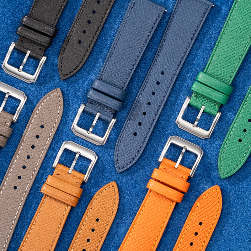 Flat lay of Epsom leather watch straps in multiple colors with stainless steel buckles on blue suede background