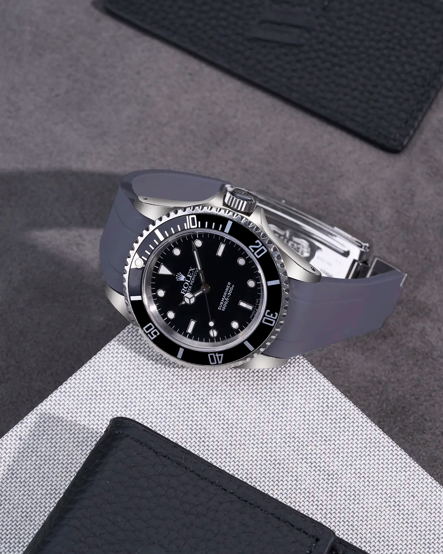 Rolex Submariner 16610 and 14060 with grey integrated FKM rubber strap and original clasp on textured surface