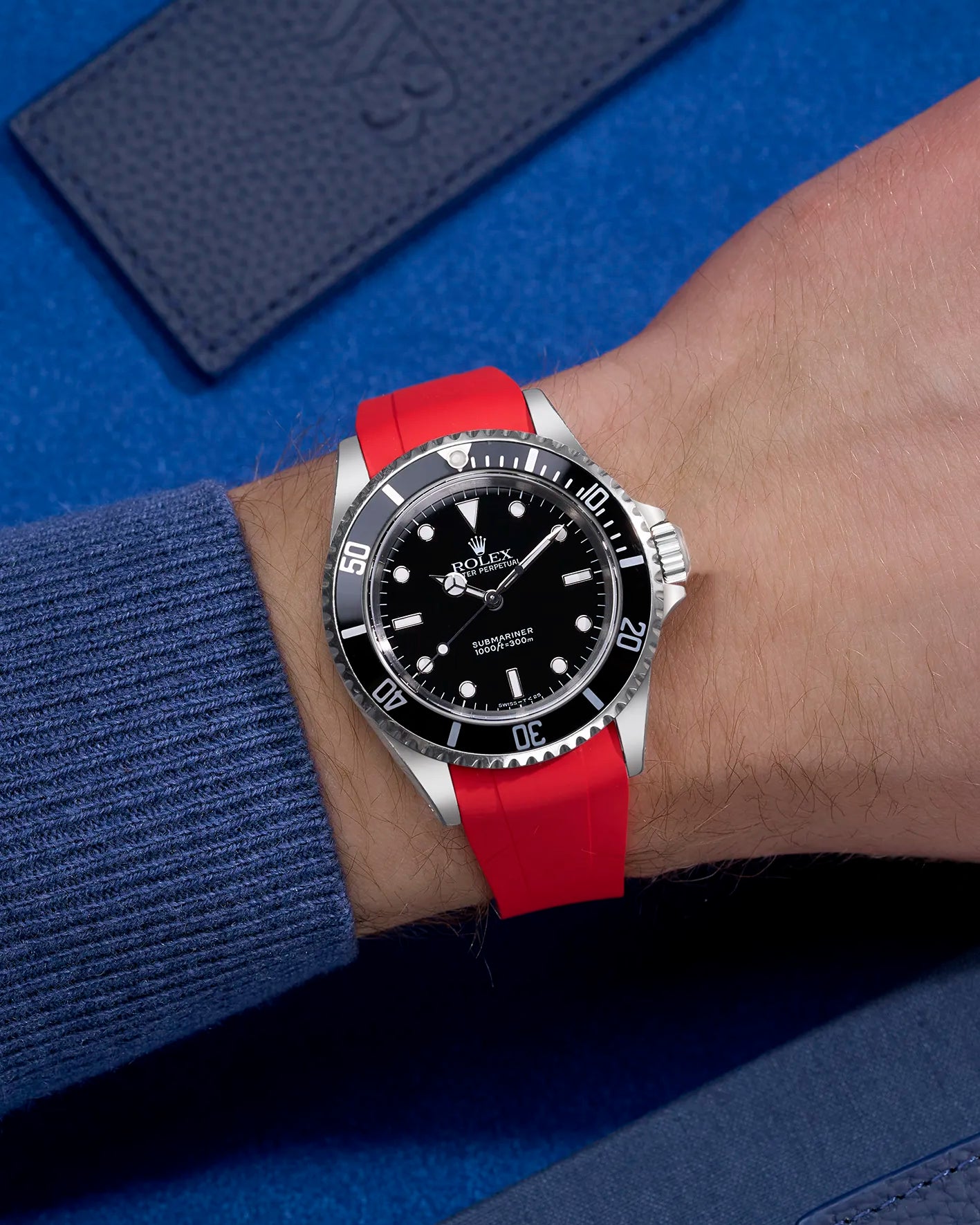Rolex Submariner 16610 and 14060 on red FKM rubber strap with original clasp integration – wrist shot on blue background