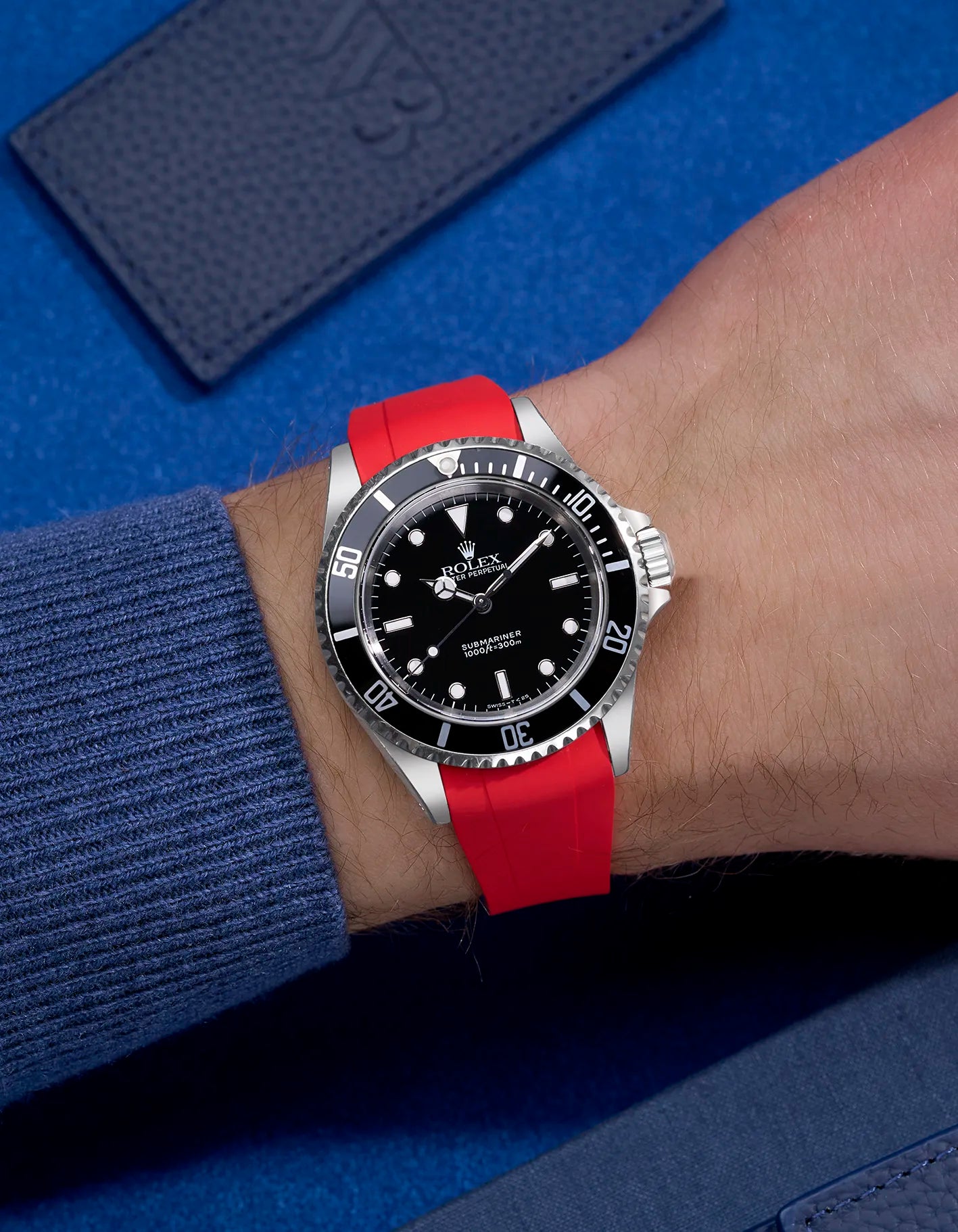 Rolex Submariner 16610 and 14060 on red FKM rubber strap with original clasp integration – wrist shot on blue background
