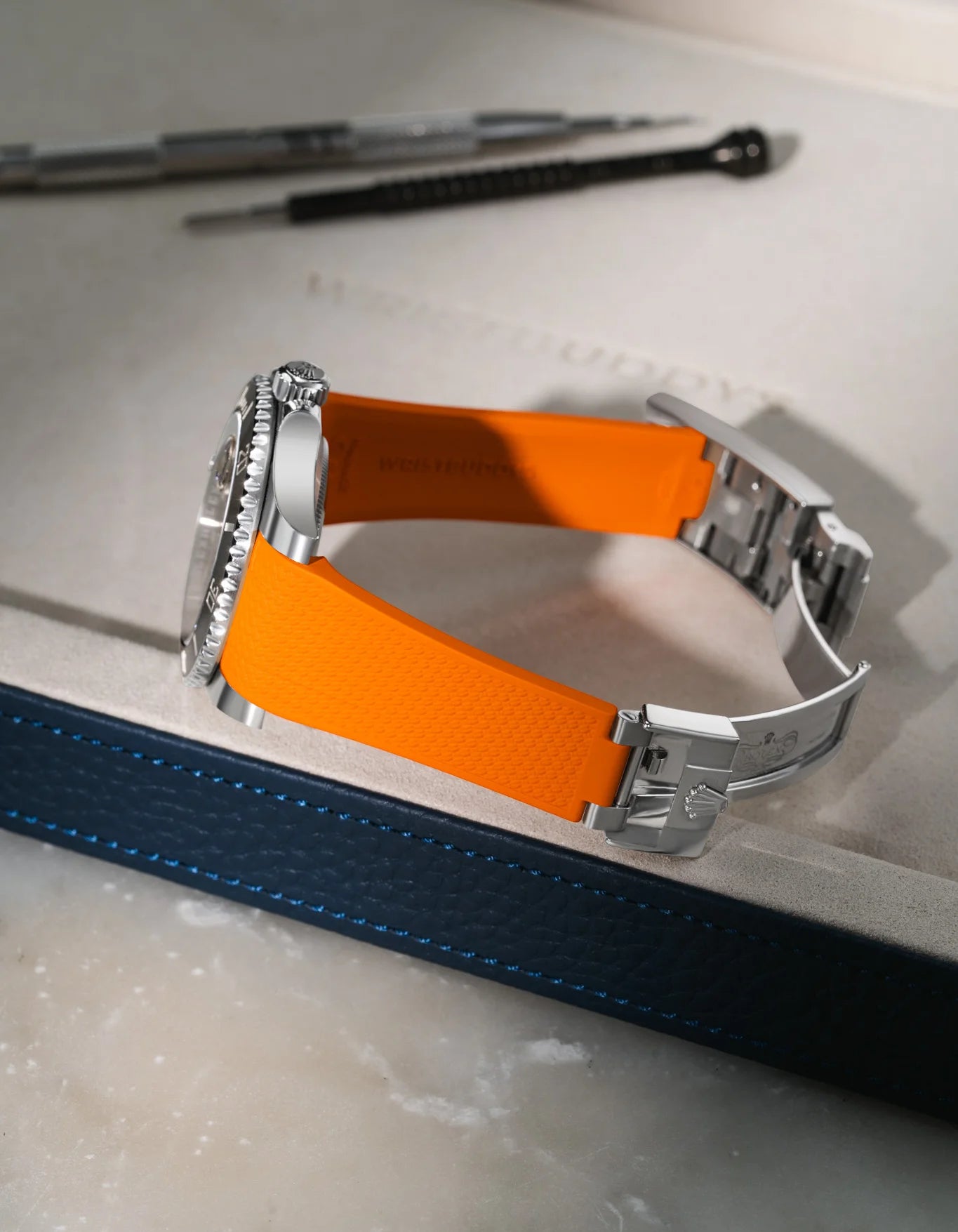 Orange Vertech FKM rubber strap for Rolex Submariner 116610 and 126610, integrated fit for original clasp, resting on a blue leather valet tray.