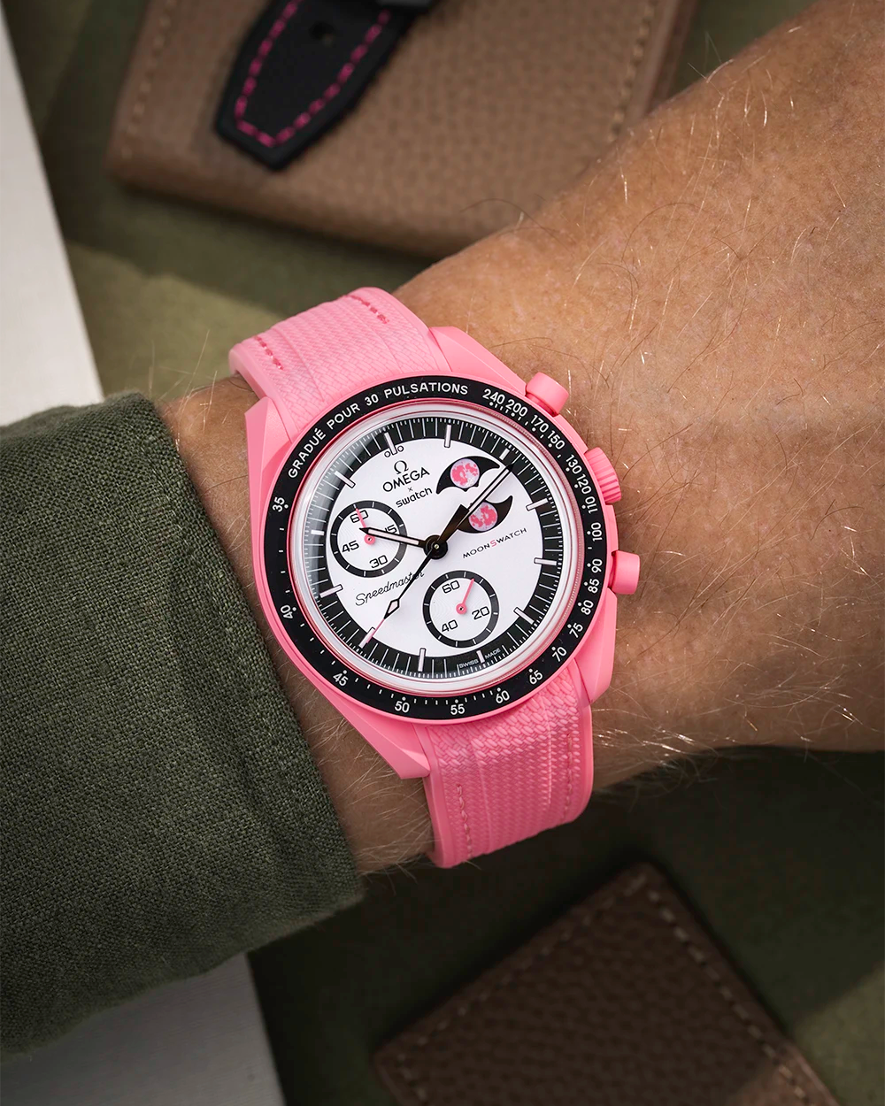 Pink watch with a detailed face on a wrist, worn by a person in a green sleeve.