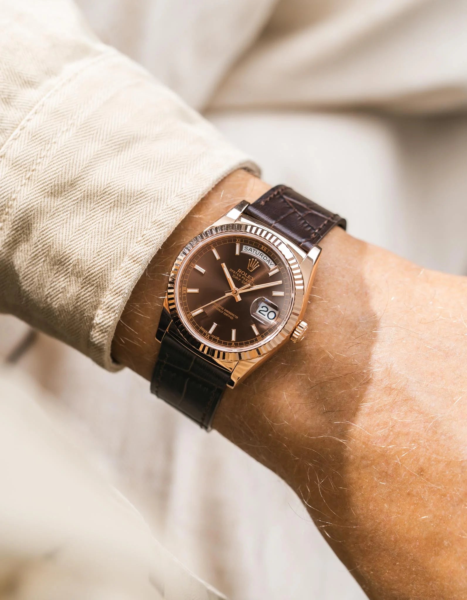 Close-up of a wrist wearing a Rolex DayDate in rose gold with a brown lallligator eather strap and brown dial.