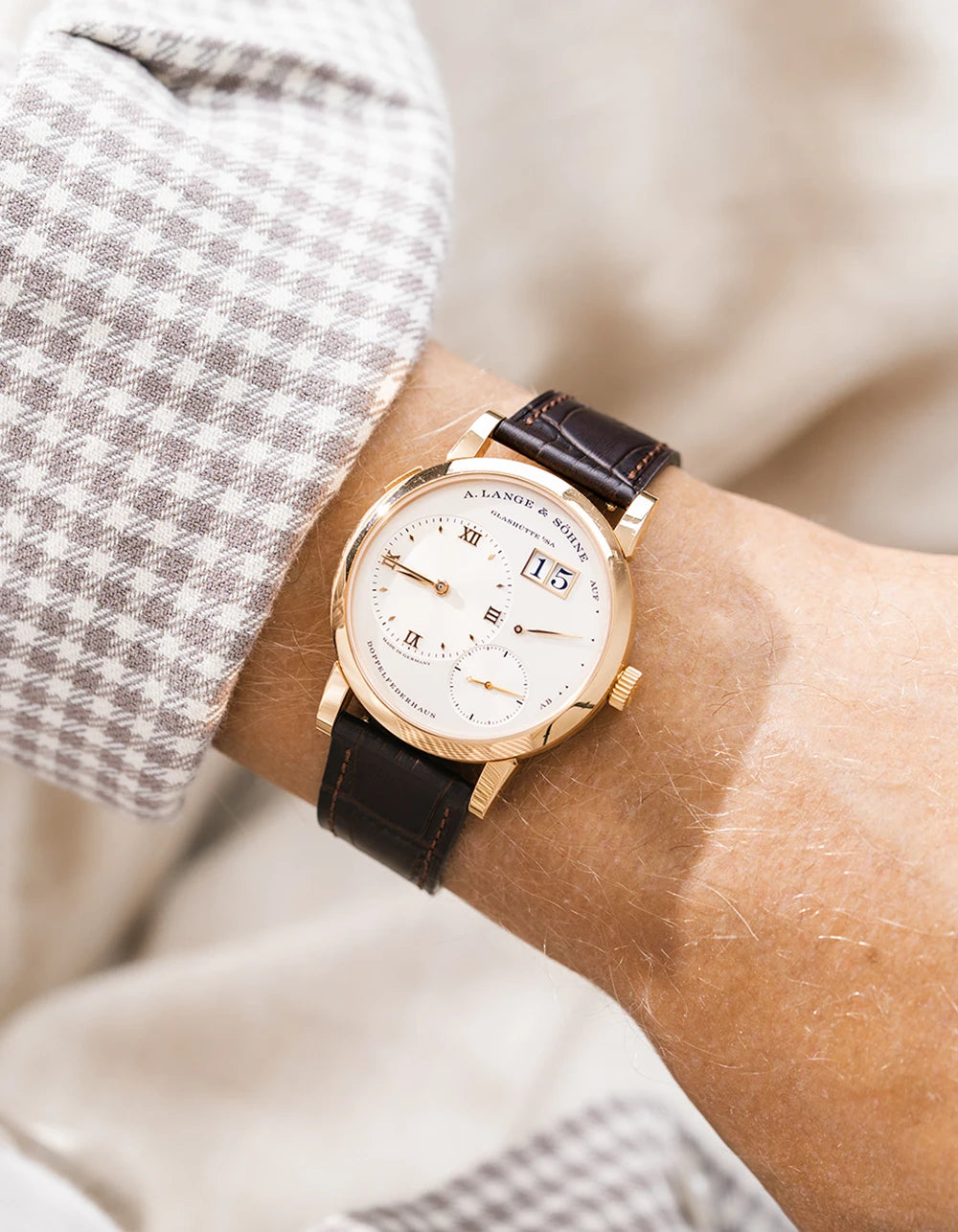 A Lange Shöne in rose gold with a dark brown embossed alligator leather strap from Wristbuddys on a wrist, wearing a green sleeve.