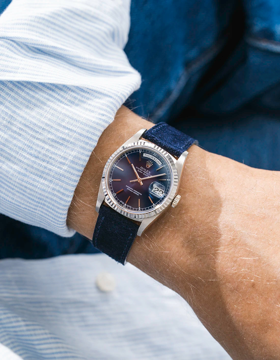 Rolex DayDate in white gold with a blue suede leather strap from Wristbuddys on a wrist, wearing a blue white sleeve.