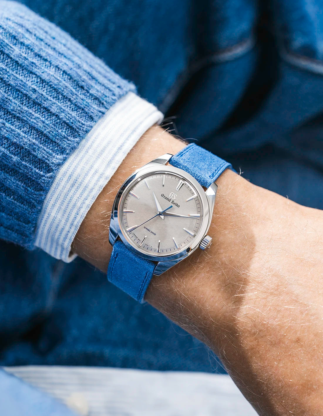 Grand Seiko with a ocean blue suede leather strap from Wristbuddys on a wrist, wearing a blue sleeve.