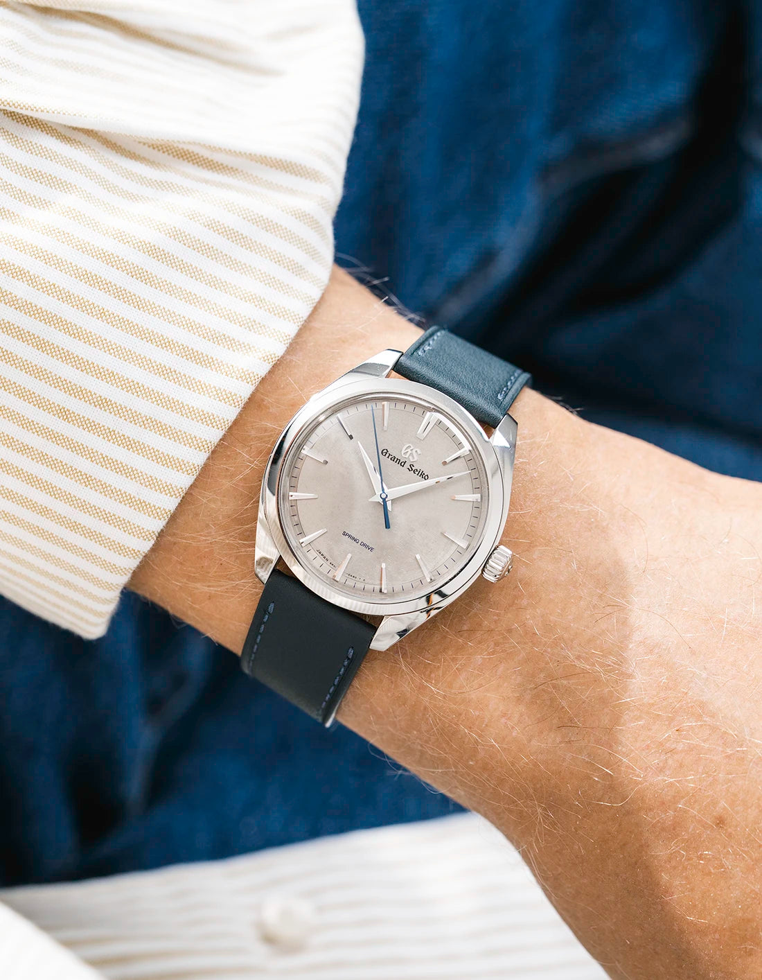 Grand Seiko with a petroleum green calfskin leather watch strap from Wristbuddys on a wrist, wearing a beige sleeve.