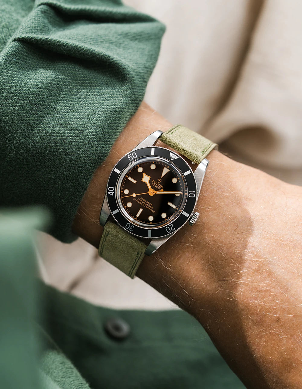 A Tudor BB54 with a herb green suede leather strap from Wristbuddys on a wrist, wearing a blue sleeve.