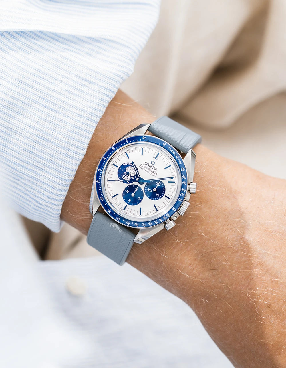 Grey straight end FKM Rubber watch strap from Wristbuddys on a Omega Speedmaster Snoopy with a blue bezel and white dial on a persons wrist close up.