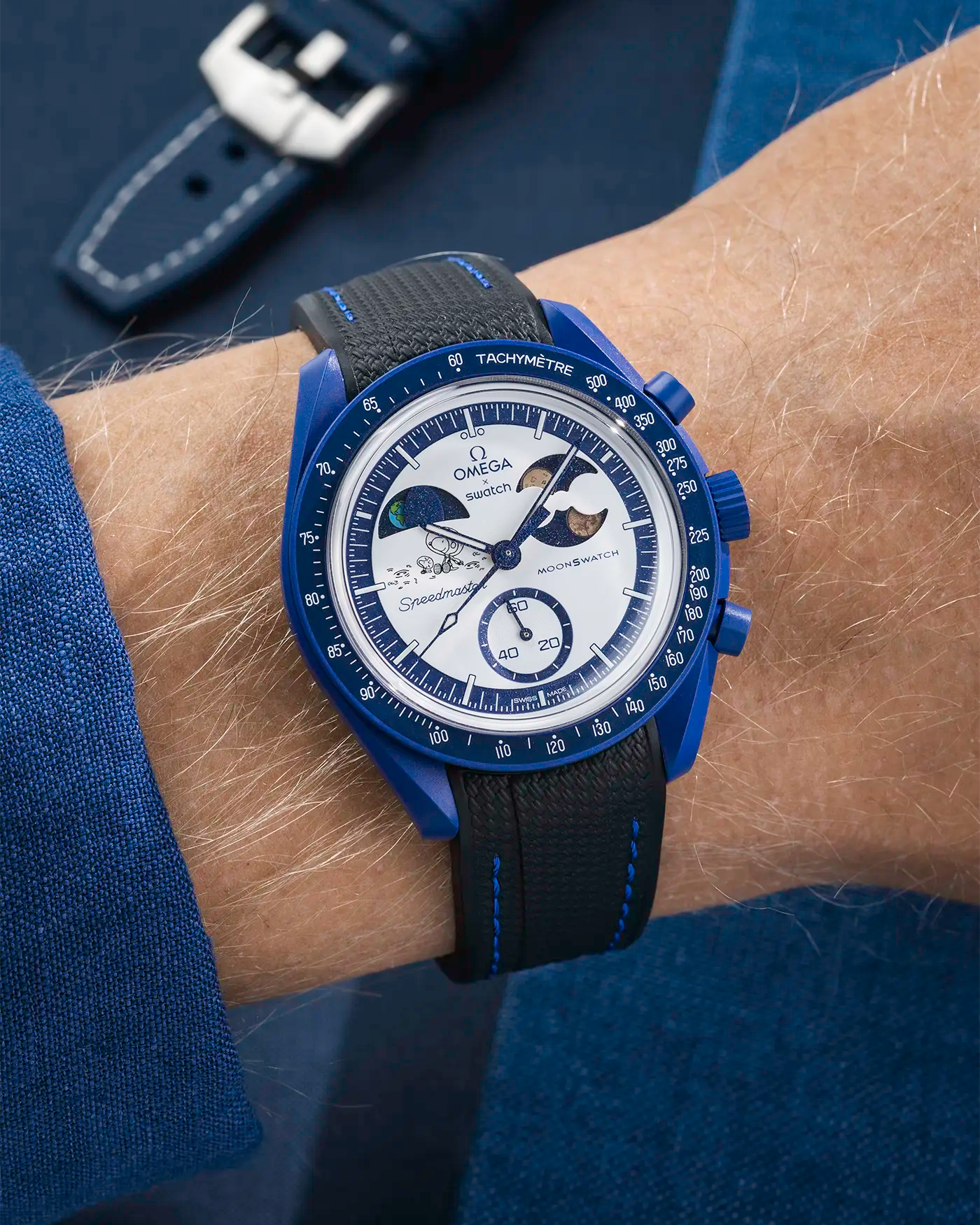 MoonSwatch Mission to Earthphase – Moonshine Gold with black rubber strap and blue stitching, wrist shot over blue background
