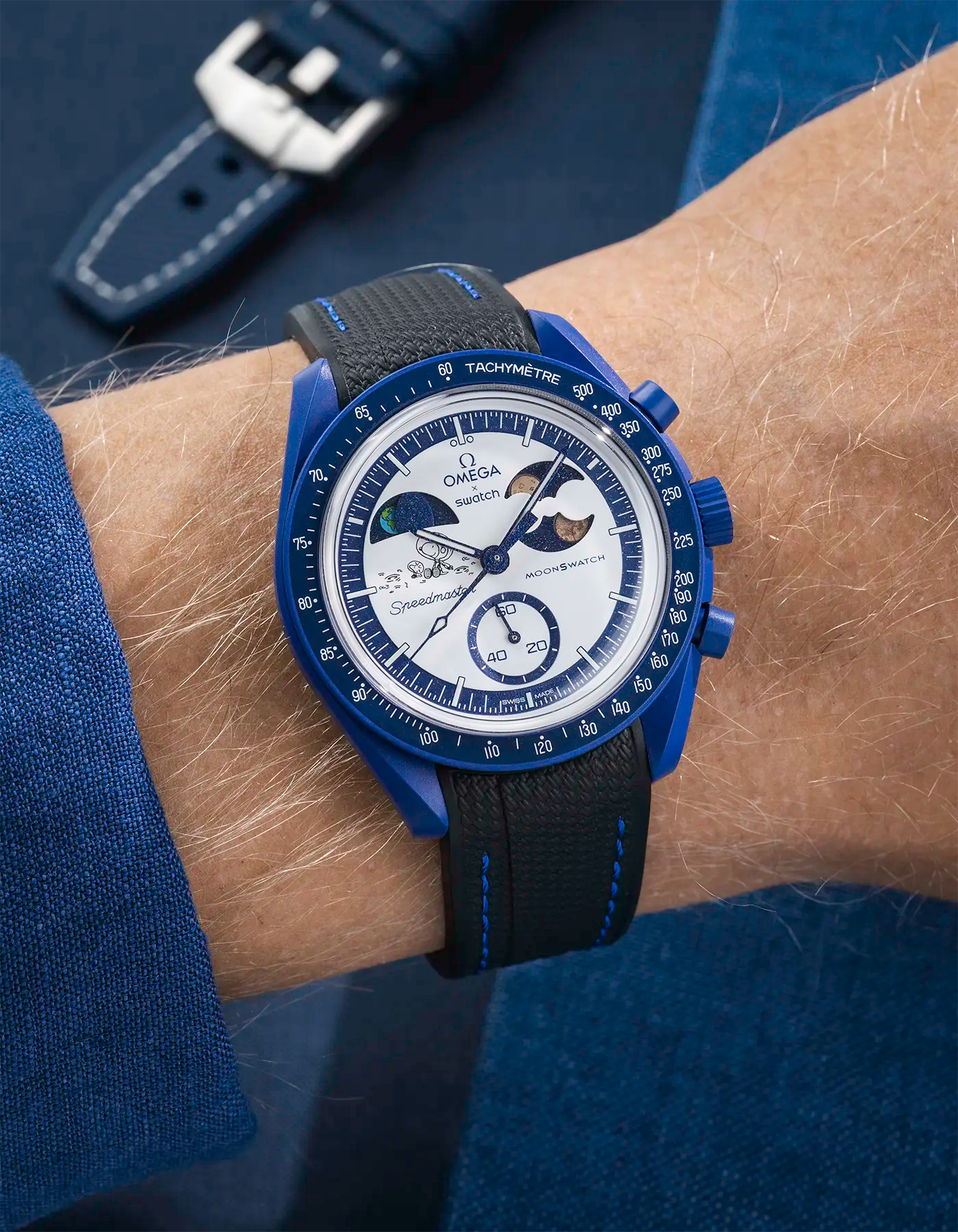 MoonSwatch Mission to Earthphase – Moonshine Gold with black rubber strap and blue stitching, wrist shot over blue background