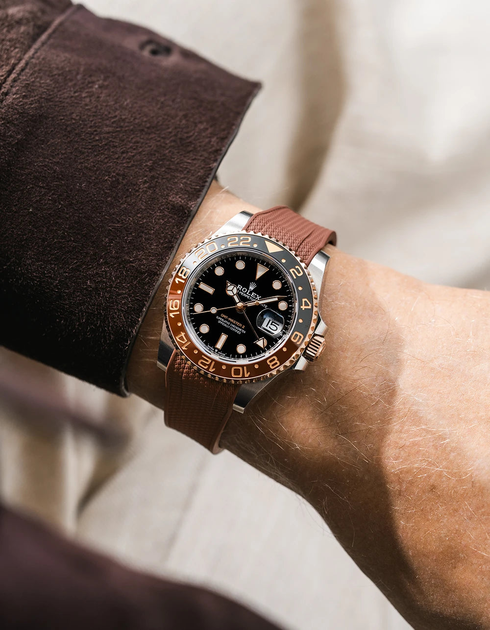 Close-up of a person wearing a Rolex GMT Master 2 Rootbeer with a brown vertech FKM rubber watch strap from Wirstbuddys on a wrist, wearing a striped shirt.