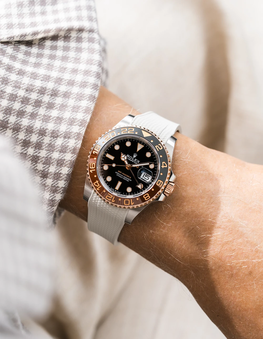 Close-up of a person wearing a Rolex GMT Master 2 Rootbeer with a beige vertech FKM rubber watch strap from Wirstbuddys on a wrist, wearing a striped shirt.