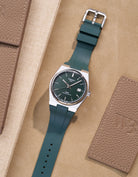 Tissot PRX watch with green dial fitted with matching green FKM rubber strap lying flat on beige background