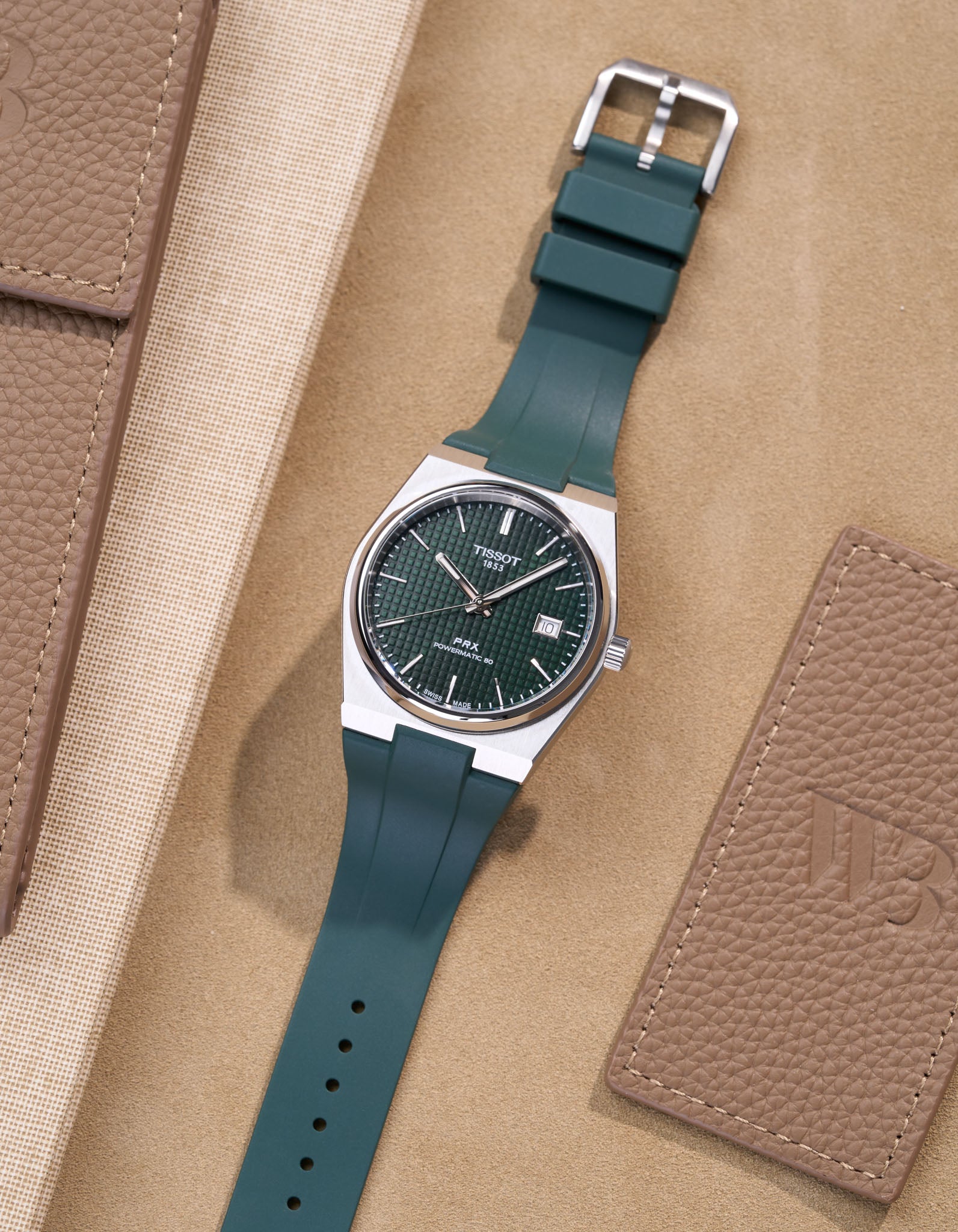 Tissot PRX watch with green dial fitted with matching green FKM rubber strap lying flat on beige background