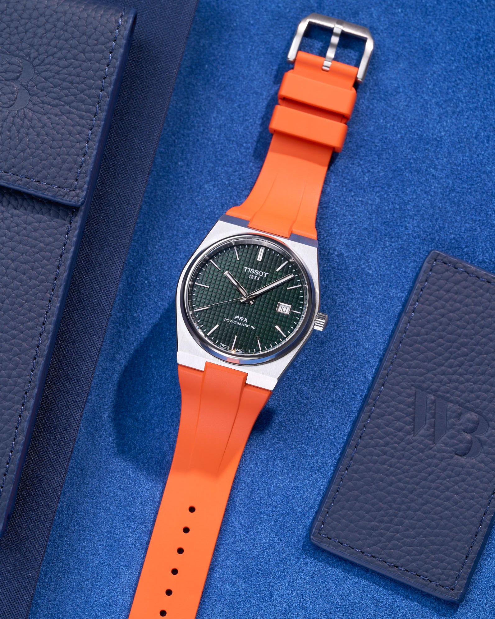 Tissot PRX watch with green dial fitted with orange FKM rubber strap lying flat on blue background