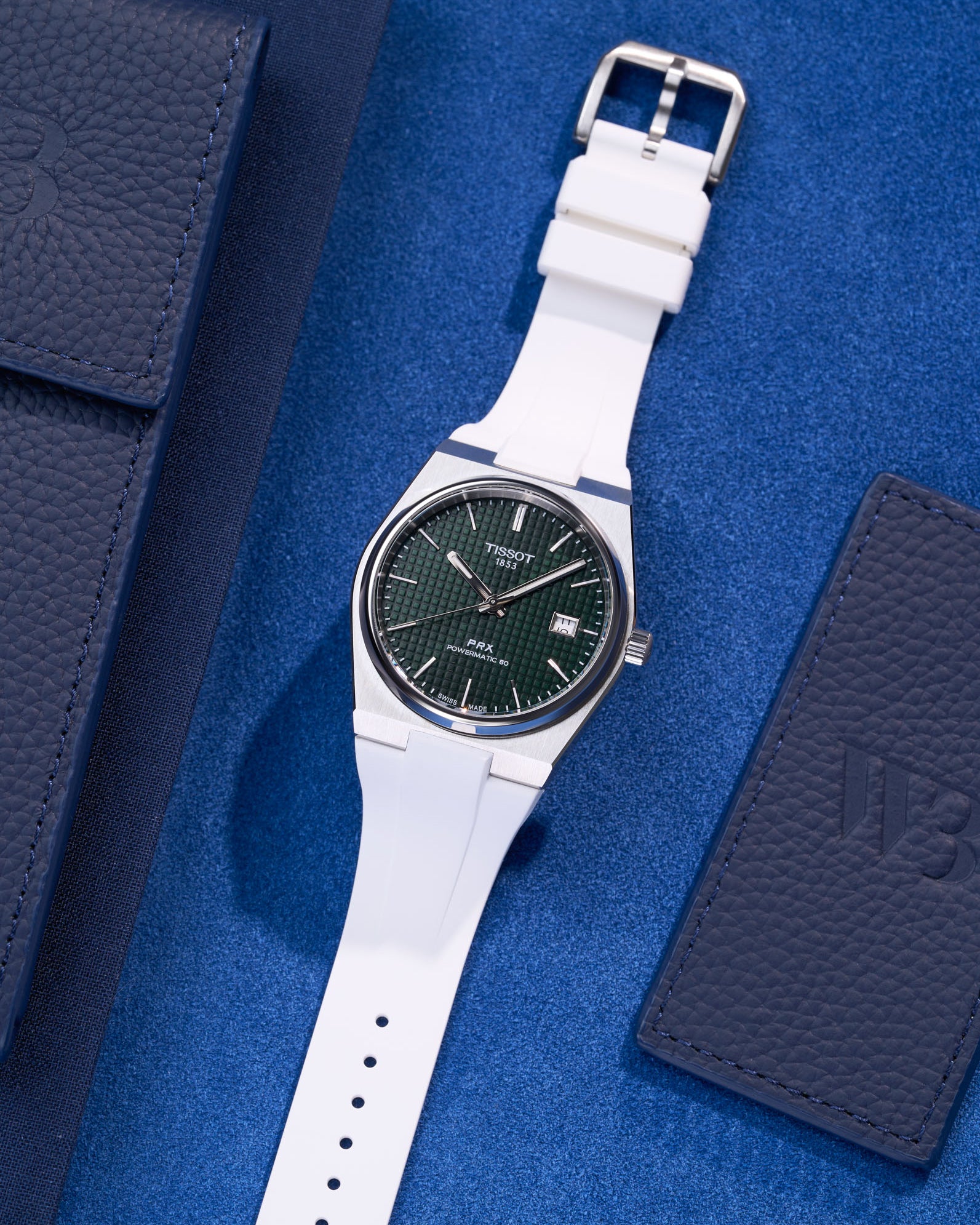 Tissot PRX Powermatic 80 with white FKM rubber strap on blue textured background flat lay