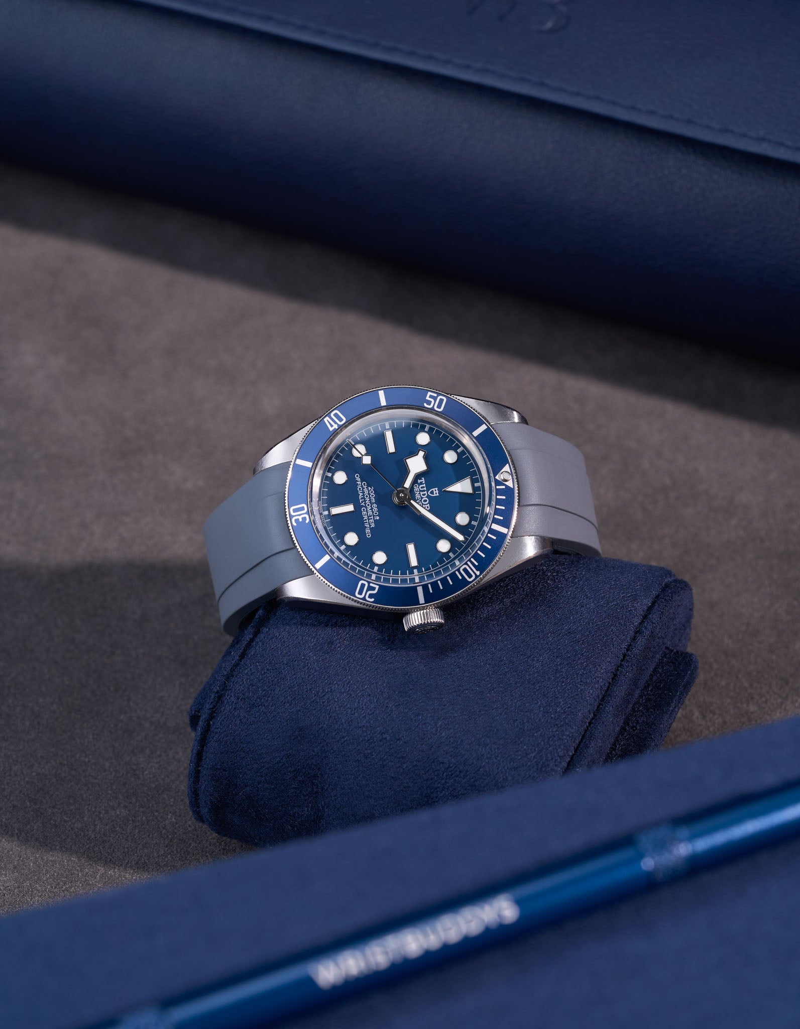 Tudor Black Bay 58 with grey FKM rubber strap attached, lying flat on blue cushion with matching accessories