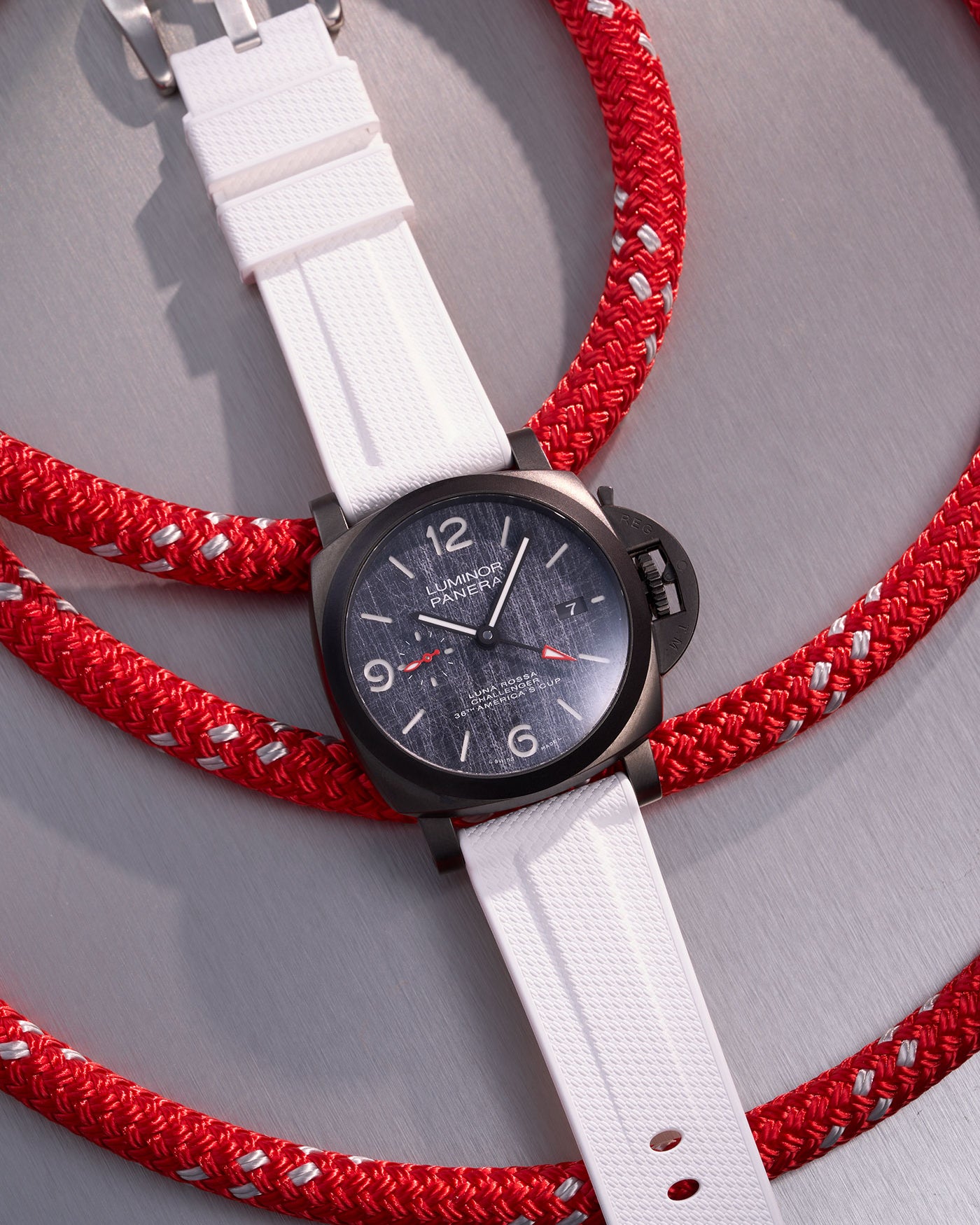 Panerai Luminor GMT Tactical Black Dial with White Rubber Strap against Red Nautical Ropes – Swiss Made luxury watch in matte black case and 24mm premium white rubber uhrenband, ideal for adventurous spirits who seek style and resilience. This Panerai replacement strap adds a fresh, contrasting look, enhancing the watch's rugged appeal for both formal and outdoor settings, ensuring durability and water resistance suitable for maritime environments