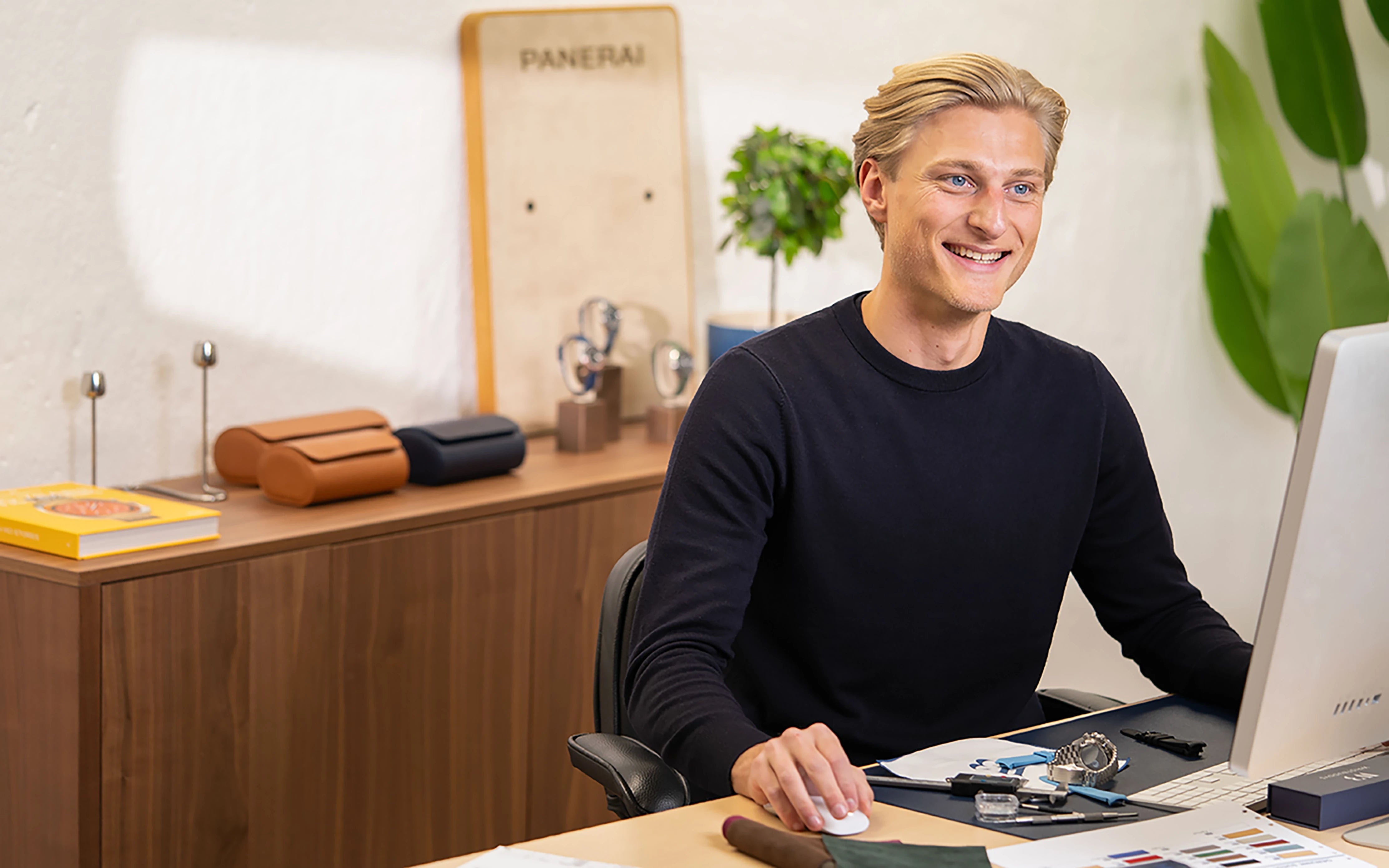 The founder of Wristbuddys, Samuel Lavatt, smiling at his desk while designing luxury watch straps – showcasing suede watch rolls and Panerai timepieces in a Scandinavian workspace